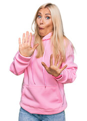 Poster - Young blonde woman wearing casual sweatshirt afraid and terrified with fear expression stop gesture with hands, shouting in shock. panic concept.