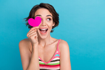 Poster - Photo of funny young girl bob hair wear singlet surprised look cover her eye pink postcard heart symbol isolated on blue color background