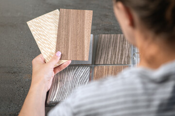 A woman holds samples of different shades for the floor in her hands, or chooses it from a designer using wooden samples.