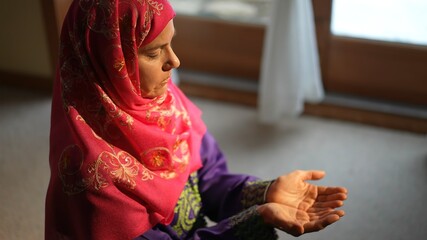 Wall Mural - Mature Muslim woman praying at home with beautiful light with snow on the ground. Concept of female prayer in home environment.