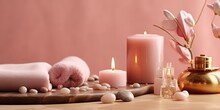 Beauty Treatment Items For Spa Procedures On Pink Wooden Table And Gold Marble Wall. Massage Stones, Essential Oils And Sea Salt. Candle, Rolled Up White Towel, Plants, Copy Space