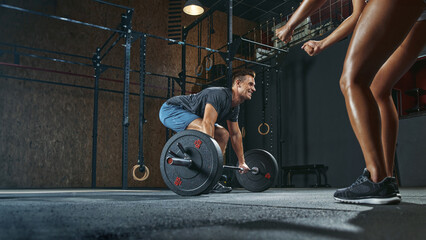 Handsome athletic man having weight training in gym motivated by female trainer or team