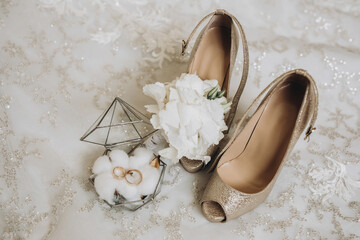 details of the bride's clothes. gold wedding rings in a glass decorative box standing on cotton flowers. Wedding flower of the groom. Women's high-heeled shoes of golden color