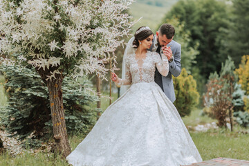 Wall Mural - European wedding couple in the park near the stairs. The bride in a beautiful dress with a long train and sleeves. Groom in a classic suit