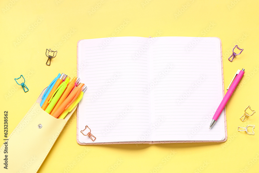 Case with colorful pens and blank notebook on yellow background
