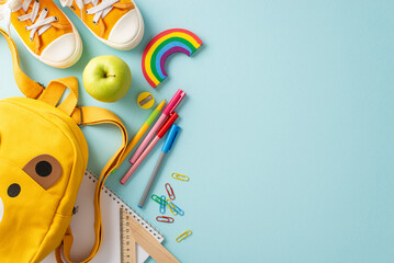 Sticker - Educational treasures for little ones. Top-down view of yellow rucksack filled with assortment of bright school supplies and shoes on pastel blue isolated backdrop, perfect for text or advertisements