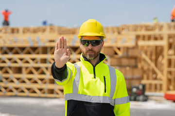 Stop, hand gesture. Worker near american wood frame house construction. American wooden house in beams, wood frame structure, framing construction.