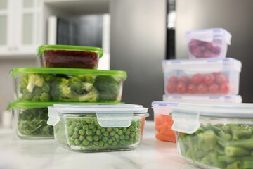 Containers with different fresh products on white marble table in kitchen, closeup. Food storage