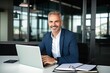 © Adriana - Smiling mature adult business man executive sitting at desk using laptop. Happy busy professional mid aged businessman ceo manager working on computer corporate technology in office