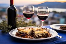  Two Plates Of Delicious Moussaka, A Classic Greek Layered Eggplant And Meat Dish, Paired With Two Glasses Of Full-bodied Greek Agiorgitiko Red Wine
