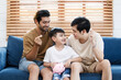 Happy LGBTQ+ gay family with adopted little son stay together in living room and teaching their adopted son about wealth and saving money for future. Diversity in gender and lifestyle concept.