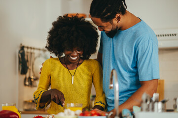 Wall Mural - A cheerful interracial couple is cooking a meal together at home.