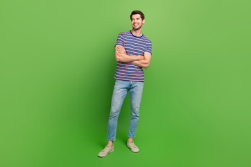 Wall Mural - Full length photo of cheerful dreamy man dressed striped t-shirt arm folded looking empty space isolated green color background