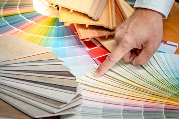 Wall Mural - Designer hand choosing and pointing at color swatch with wood laminate material samples and wooden tile texture collection nearby. Catalog guide for interior architecture and furniture design work