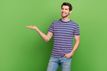 Sticker - Photo of young promoter advertiser man holding arm proposition object look interested commerce deal isolated on green color background