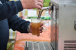 Cold draught beer is poured from a mobile tap in a plastic glass at an open air summer festival, copy space, selected focus