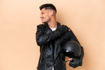 Wall Mural - Young caucasian man with a motorcycle helmet isolated on beige background suffering from pain in shoulder for having made an effort