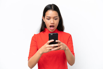 Wall Mural - Young Colombian woman isolated on white background looking at the camera while using the mobile with surprised expression