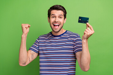 Poster - Photo of overjoyed funny young businessman successful entrepreneur premium wireless card fist up hooray isolated on green color background