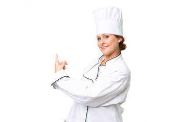 Wall Mural - Middle-aged chef woman over isolated background pointing back