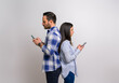 © Moon Safari - Side view of serious young couple standing back to back and text messaging over smart phones. Man and woman dressed in casuals checking social media on cellphones against background