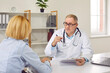 Young woman having consultation with mature male doctor in medical office. Professional therapist, general practitioner giving prescription to blonde woman at visit. Medicine, healthcare