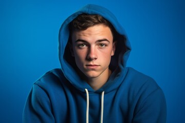 Wall Mural - Photography in the style of pensive portraiture of a satisfied boy in his 20s wearing a comfortable hoodie against a royal blue background. With generative AI technology