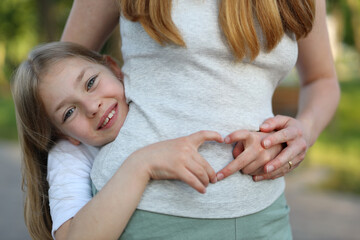 Wall Mural - Portrait of a happy daughter who loves and hugs her mother, shows a symbol of the heart.