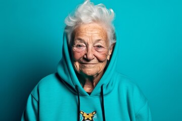 Poster - Close-up portrait photography of a glad old woman wearing a stylish hoodie against a teal blue background. With generative AI technology