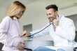 © Home-stock - Cheerful male doctor listening to baby heart during young lady appointment in hospital, female patient visiting her gynecologist in clinic