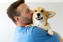 Friendly Man Veterinarian Holding On Hands And Kissing Cute Pembroke Welsh Corgi Dog During Examination In The Clinic, Closeup Shot