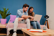 © Jose Calsina - Happy young couple watching the laptop screen, checking finances, planning budget or mortgage sitting at couch of their apartment. Smiling husband showing on his wife's notebook a online shopping sale