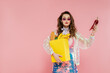 housewife concept, attractive young woman in sunglasses carrying paper bag with groceries and holding red pepper, posing like a doll on pink background, conceptual photography, home duties