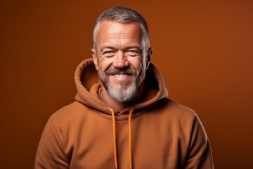 Wall Mural - Medium shot portrait photography of a grinning mature man wearing a stylish hoodie against a copper brown background. With generative AI technology