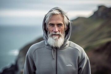 Wall Mural - Sports portrait photography of a satisfied old man wearing a comfortable hoodie against a dramatic coastal cliff background. With generative AI technology