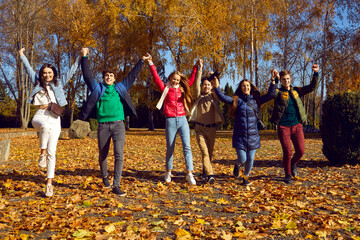 Happy friends raising their hands together in public park. Group of young people wearing warm clothes walking together in sunny autumn day. Friendship, positive, optimistic people