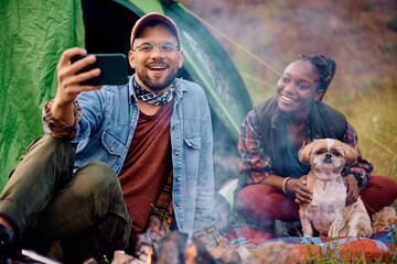 Happy couple with dog takes selfie while camping in nature.