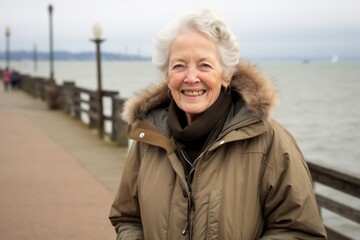 Wall Mural - Environmental portrait photography of a satisfied old woman wearing a durable parka against a scenic beach pier background. With generative AI technology