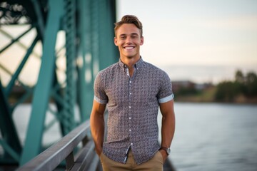 Wall Mural - Urban fashion portrait photography of a happy boy in his 30s wearing a casual short-sleeve shirt against a picturesque bridge background. With generative AI technology