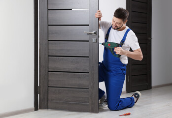 Poster - Worker in uniform with screw gun repairing door lock indoors