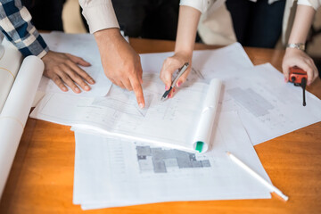 Wall Mural - Hand shot of 3 engineers. Man and woman pointing at a blueprint with a pen on a workbench. A walkie talkie and a pencil nearby, wearing a uniform, designing a construction industry. in office work