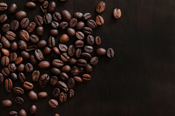 Wall Mural - Roasted coffee beans on a wooden dark table, top view. Background of fragrant brown coffee beans scattered over the surface. Copy space