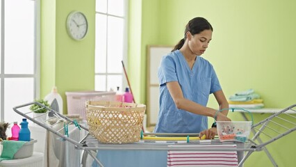 Poster - African american woman professional cleaner hanging clothes on clothesline looking watch at laundry room