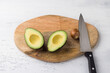 Fresh avocado cut in half and avocado pit with a knife on a wooden board on a light gray background, top view