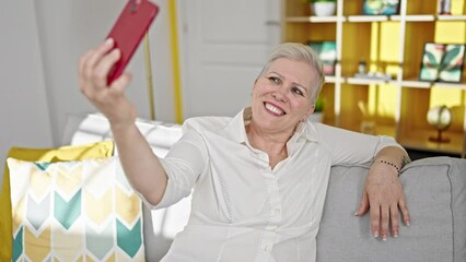 Poster - Middle age grey-haired woman taking selfie picture with smartphone sitting on the sofa at home