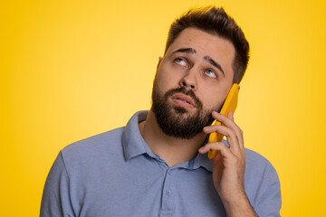 Disinterested young Caucasian man having annoyed boring talk on smartphone. Tired sleepy adult guy talking on mobile phone with friend, making online conversation isolated on studio yellow background