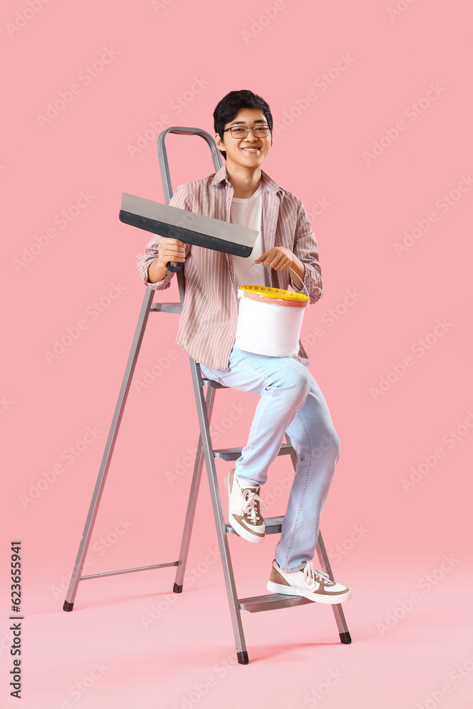 Young Asian man with putty knife and plaster on pink background
