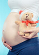© ratmaner - Woman in pregnant holding teddy bear for her expected child. Expecting for newborn. Extending family