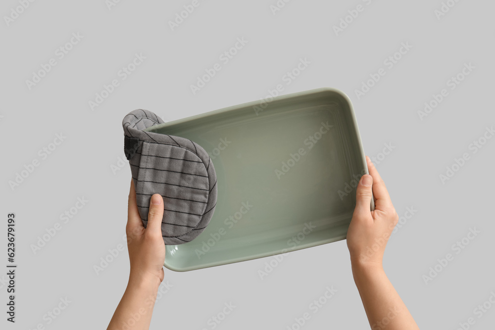 Female hands with baking form and mitt on grey background