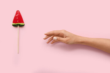 Wall Mural - Female hand with lollipop in shape of watermelon slice on pink background